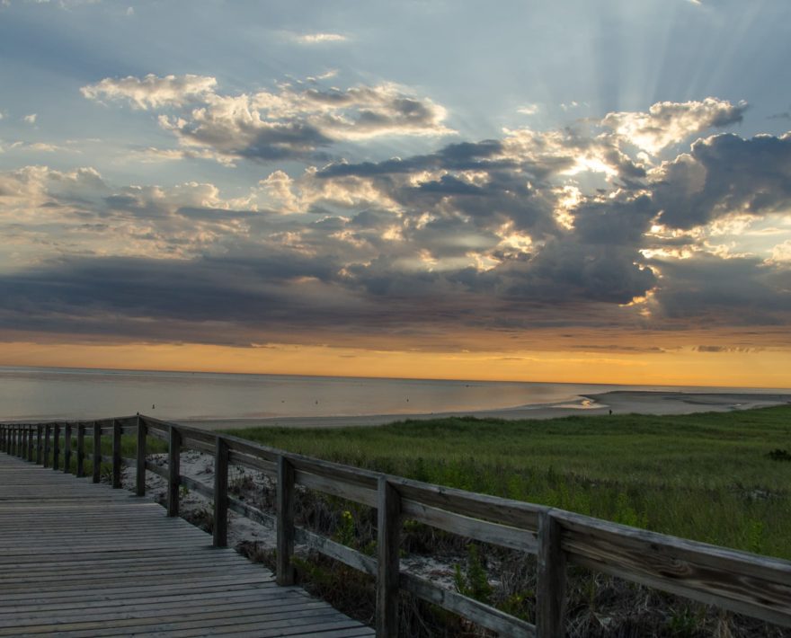 Sun rays through the clouds viewed from the boardwalk to Crane Beach at sunrise